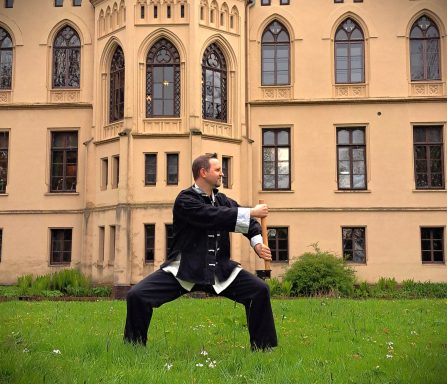 Mann in traditioneller Kleidung übt Tai Chi vor einem historischen Gebäude.