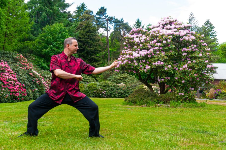 Mann in traditioneller Kleidung übt Tai Chi in einem blühenden Garten.