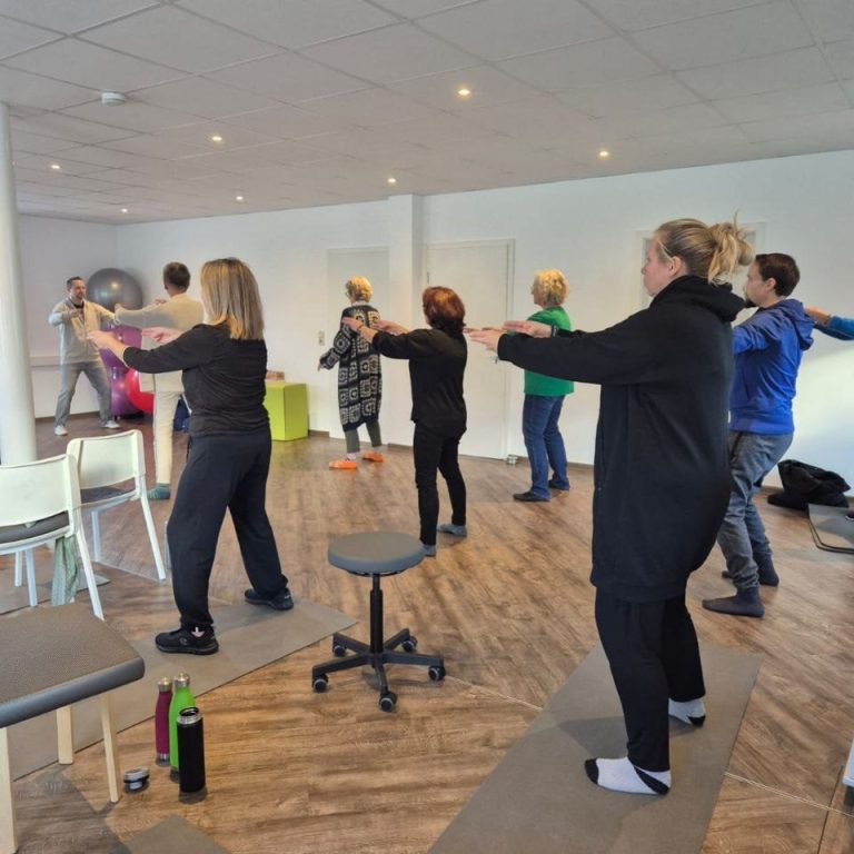 Eine Gruppe von Personen macht gemeinsam Fitnessübungen in einem hellen Raum.