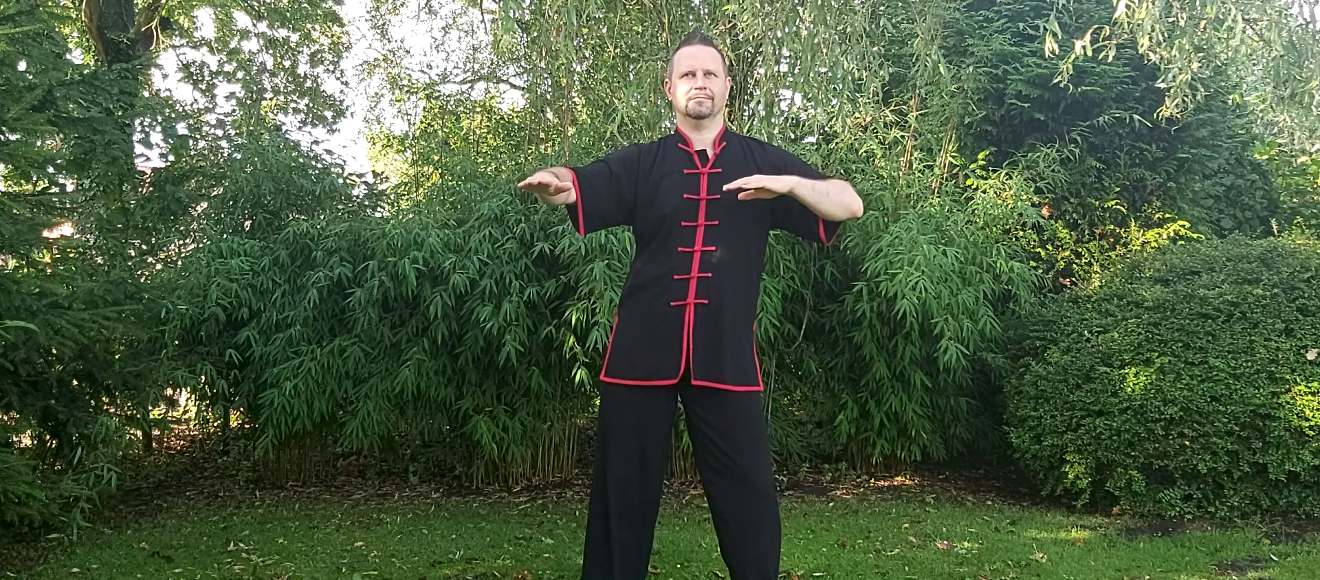 Ein Mann in einer schwarzen, roten gesäumten Kleidung übt Tai Chi im Freien.