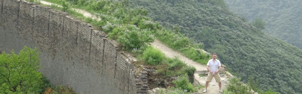 Mann steht auf einem felsigen Weg entlang einer grünen Bergwand.