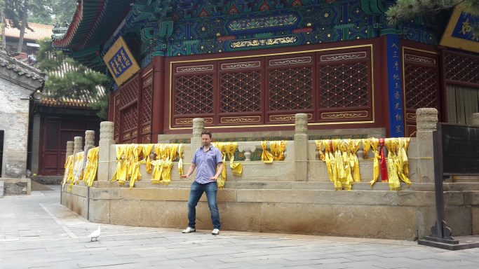 Mann steht vor einem Tempel mit gelben Stoffbändern und kunstvoll verziertem Hintergrund.