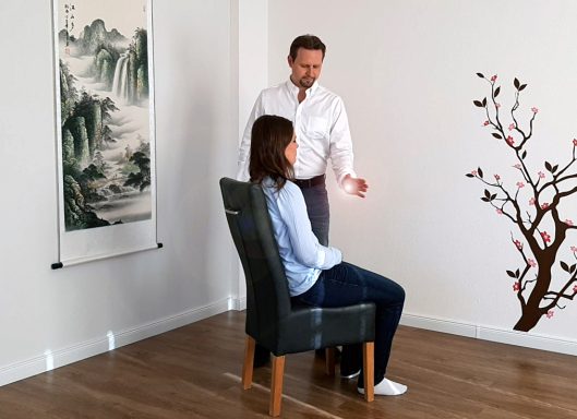 Ein Mann steht neben einer sitzenden Frau in einem hellen Raum mit Pflanzenmotiven.