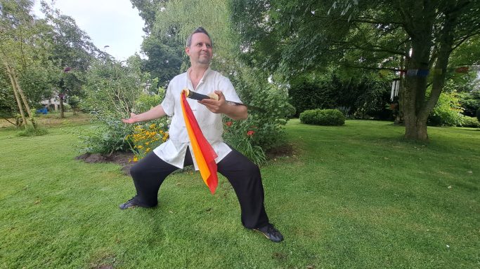 Mann in Garten mit Tai Chi Kleidung und Schwert.