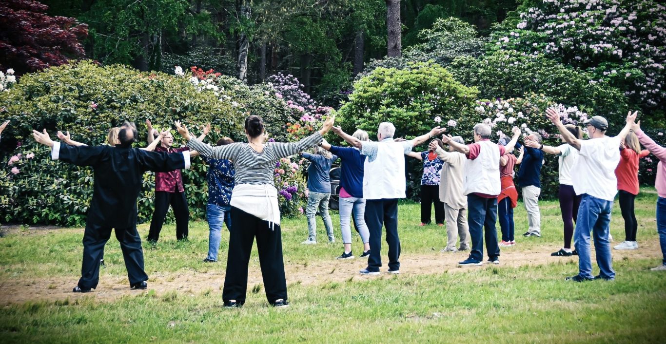 Person praktiziert Qi Gong am Strand, während verschiedene Geräte den Kurs anzeigen.