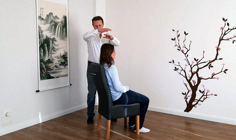 Ein Mann steht hinter einer sitzenden Frau und führt eine Behandlung aus.