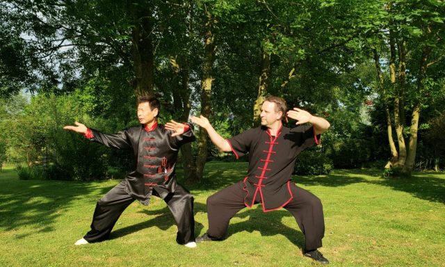 Zwei Männer in traditioneller Kampfkunstkleidung üben Tai Chi im Freien.
