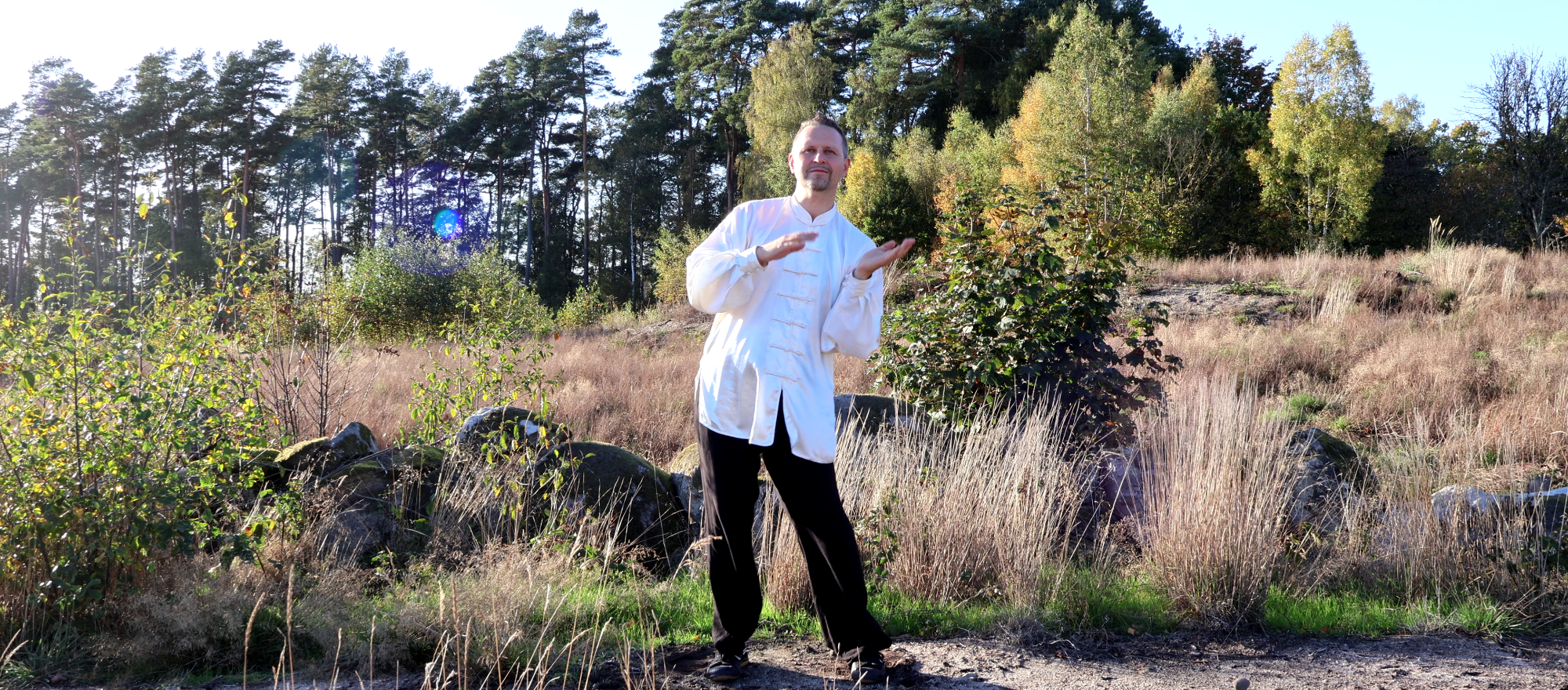 Ein Mann in einer schwarzen, roten gesäumten Kleidung übt Tai Chi im Freien.