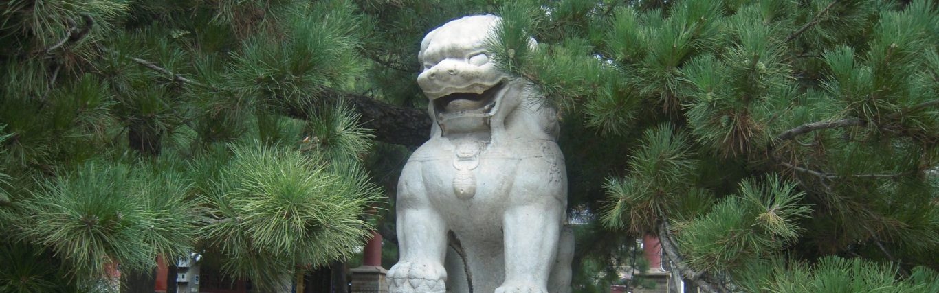 Steinfigur Löwe aus Stein, umgeben von grünen Bäumen und Pflanzen.