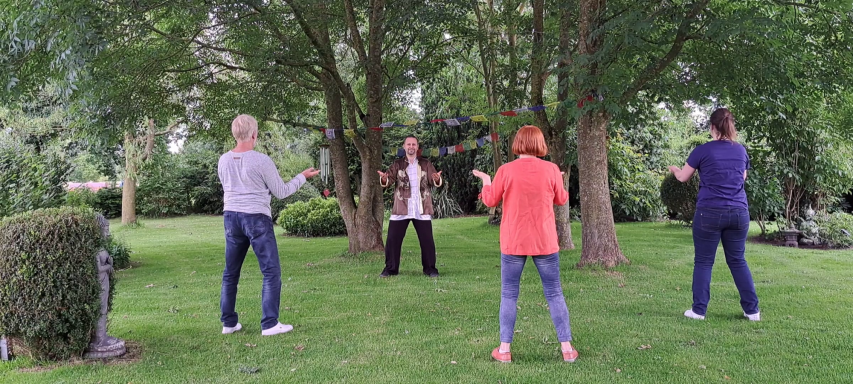 Gruppe von vier Personen beim Tai-Chi im Freien unter Bäumen.