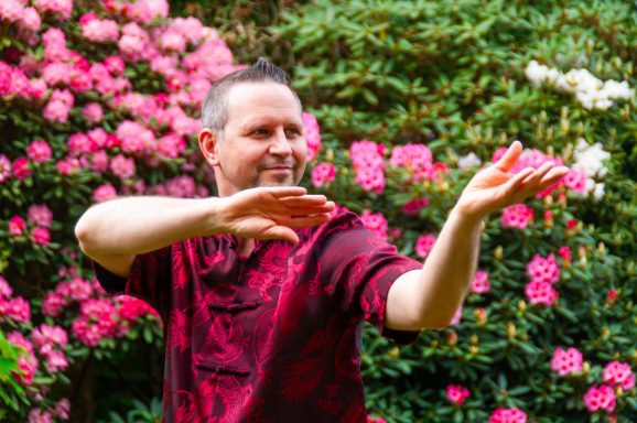 Mann in rotem Hemd führt eine gefühlvolle Bewegung vor einem Blumenhintergrund aus.